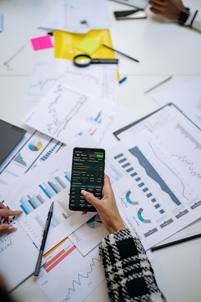 Person analyzes financial charts using a smartphone in an office setting.